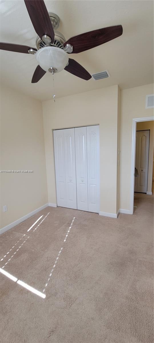 unfurnished bedroom featuring light carpet, ceiling fan, and a closet