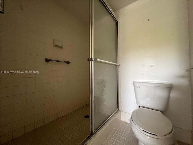 bathroom with tile patterned flooring, toilet, and a shower with shower door