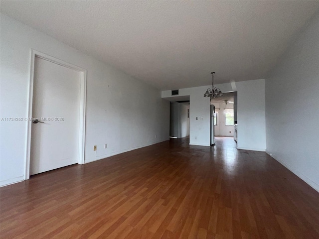 unfurnished room featuring a notable chandelier, dark hardwood / wood-style floors, and a textured ceiling