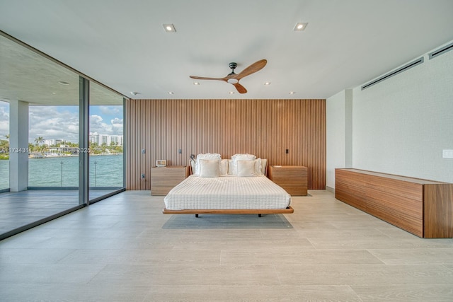 bedroom featuring ceiling fan, access to exterior, wooden walls, a water view, and expansive windows