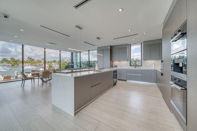 kitchen with sink, gray cabinetry, stainless steel oven, hanging light fixtures, and a large island with sink