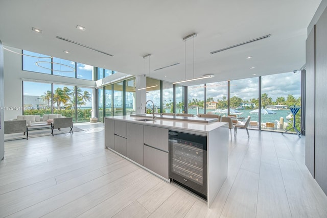 kitchen with sink, gray cabinetry, beverage cooler, a wall of windows, and a water view