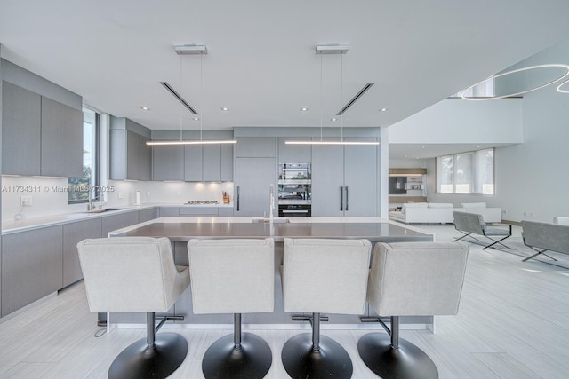 kitchen featuring sink, a breakfast bar, gray cabinetry, a spacious island, and decorative light fixtures