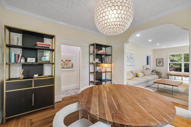 dining area with wood-type flooring, ornamental molding, and a textured ceiling