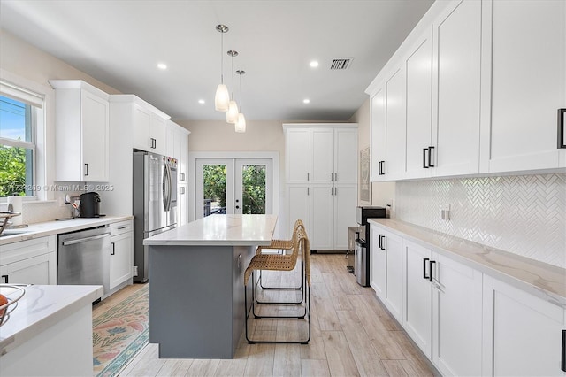 kitchen featuring french doors, a center island, hanging light fixtures, appliances with stainless steel finishes, and white cabinets