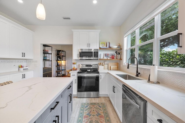 kitchen with sink, white cabinetry, decorative light fixtures, stainless steel appliances, and light stone countertops