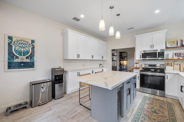 kitchen featuring white cabinetry, stainless steel appliances, light stone countertops, and a kitchen island