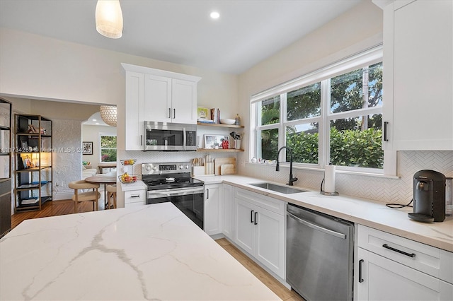 kitchen with pendant lighting, sink, white cabinetry, stainless steel appliances, and light stone counters