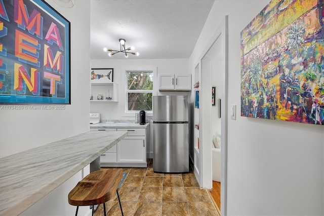 kitchen featuring stainless steel refrigerator, white cabinetry, an inviting chandelier, light stone countertops, and a textured ceiling