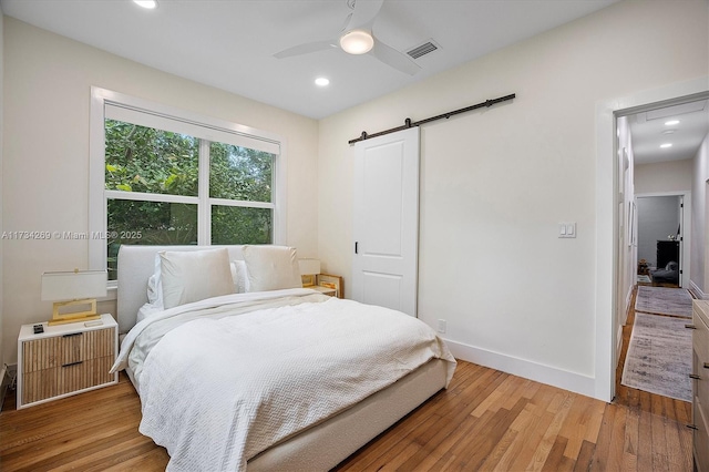 bedroom featuring radiator, light hardwood / wood-style floors, a barn door, and ceiling fan