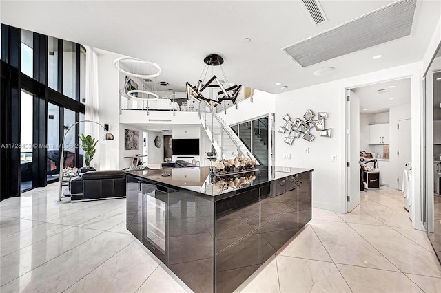 kitchen featuring white cabinetry, a large island, a towering ceiling, and decorative light fixtures