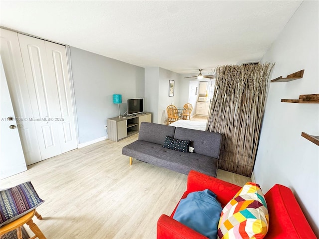 living room featuring ceiling fan, light hardwood / wood-style flooring, and a textured ceiling