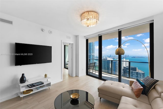 living room with an inviting chandelier, light wood-type flooring, expansive windows, and a water view