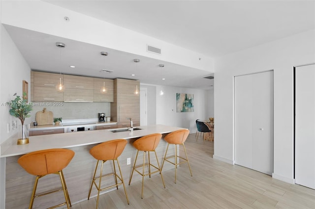 kitchen featuring sink, a breakfast bar, hanging light fixtures, light hardwood / wood-style floors, and light brown cabinets