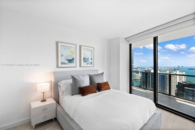 bedroom featuring access to outside, light hardwood / wood-style floors, expansive windows, and a water view