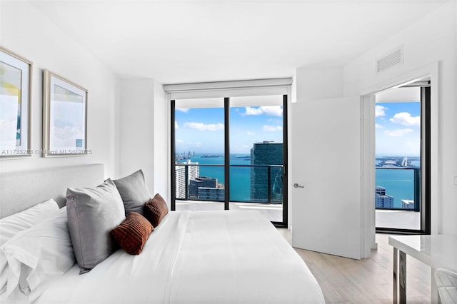 bedroom featuring a water view, access to outside, light wood-type flooring, and a wall of windows