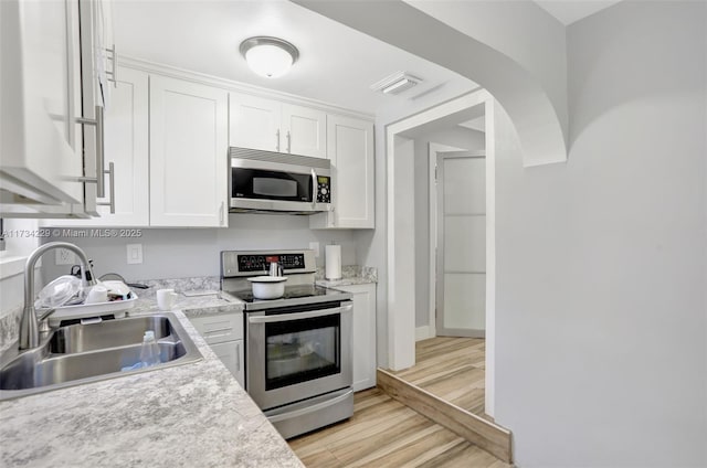 kitchen featuring sink, appliances with stainless steel finishes, light stone counters, light hardwood / wood-style floors, and white cabinets