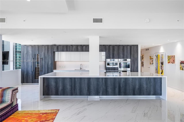 kitchen featuring white cabinetry, sink, double oven, and a large island with sink