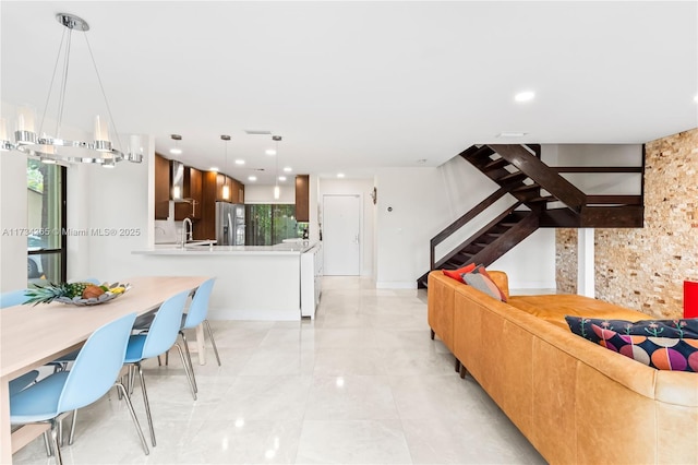 kitchen with stainless steel refrigerator with ice dispenser, wall chimney exhaust hood, sink, decorative light fixtures, and kitchen peninsula