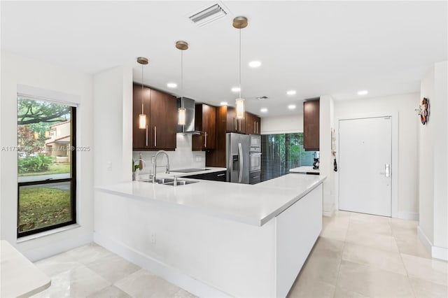 kitchen with wall chimney exhaust hood, sink, stainless steel fridge, kitchen peninsula, and pendant lighting