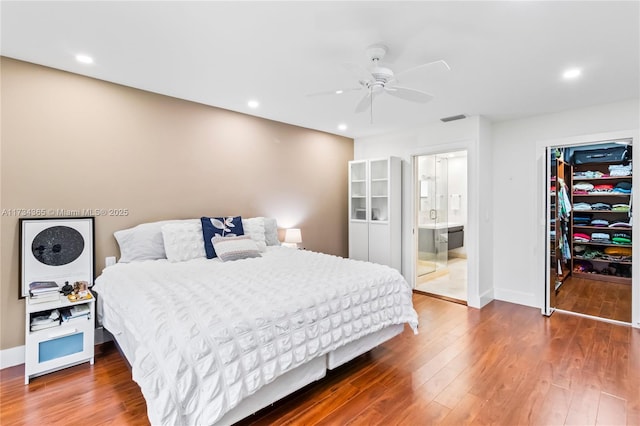 bedroom featuring a walk in closet, wood-type flooring, ensuite bath, a closet, and ceiling fan