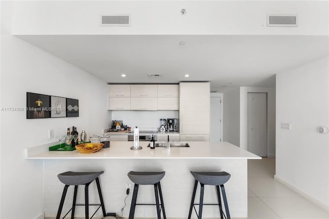 kitchen with white cabinetry, sink, light tile patterned flooring, and a kitchen bar