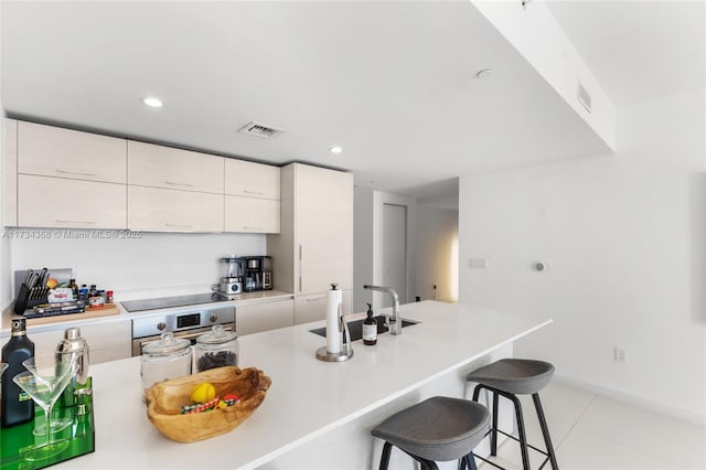 kitchen with sink, a kitchen breakfast bar, black electric stovetop, stainless steel oven, and light tile patterned floors