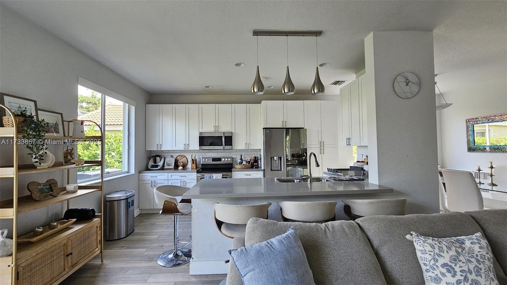 kitchen featuring appliances with stainless steel finishes, pendant lighting, sink, white cabinets, and a kitchen breakfast bar