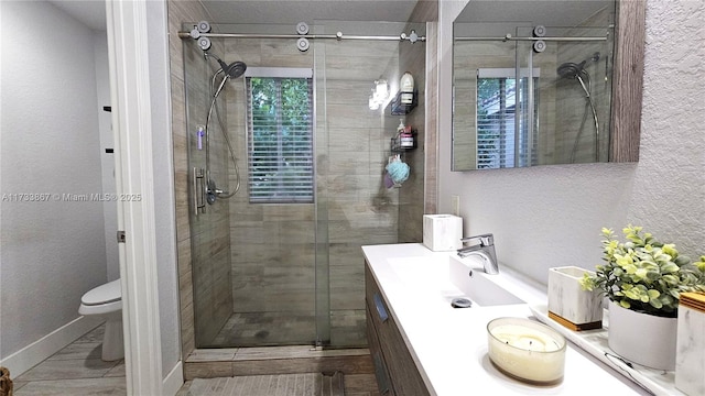 bathroom with double vanity, a stall shower, a textured wall, toilet, and a sink