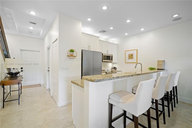 kitchen with a breakfast bar area, stainless steel appliances, light stone counters, white cabinets, and kitchen peninsula