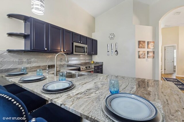 kitchen featuring vaulted ceiling, appliances with stainless steel finishes, sink, backsplash, and light stone countertops