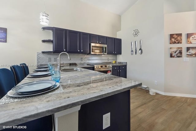 kitchen featuring light stone counters, light wood-style flooring, a sink, decorative backsplash, and appliances with stainless steel finishes