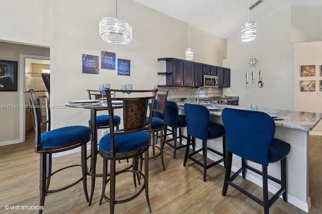 kitchen with hanging light fixtures, light hardwood / wood-style floors, kitchen peninsula, and a kitchen bar