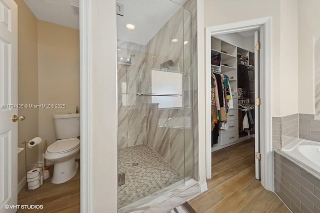 bathroom featuring a garden tub, a spacious closet, wood finished floors, and a marble finish shower