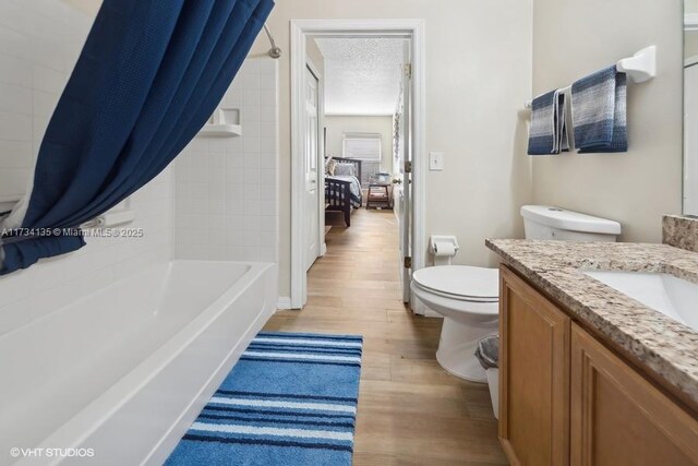 full bathroom featuring shower / bath combo, vanity, wood-type flooring, a textured ceiling, and toilet