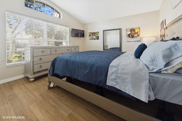 bedroom featuring lofted ceiling, multiple windows, wood finished floors, and baseboards