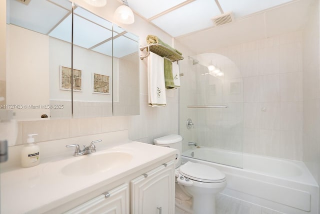 full bathroom featuring tile walls, decorative backsplash, tiled shower / bath combo, vanity, and toilet