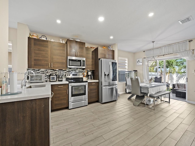 kitchen with sink, light wood-type flooring, appliances with stainless steel finishes, pendant lighting, and backsplash