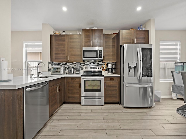 kitchen with appliances with stainless steel finishes, sink, decorative backsplash, dark brown cabinets, and light wood-type flooring