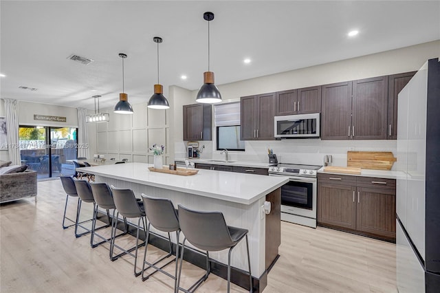 kitchen with appliances with stainless steel finishes, decorative light fixtures, a breakfast bar area, a center island, and dark brown cabinets