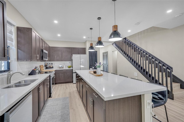 kitchen featuring a large island, sink, hanging light fixtures, stainless steel appliances, and light wood-type flooring