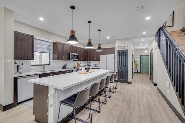 kitchen featuring a breakfast bar, appliances with stainless steel finishes, dark brown cabinets, a center island, and light hardwood / wood-style floors