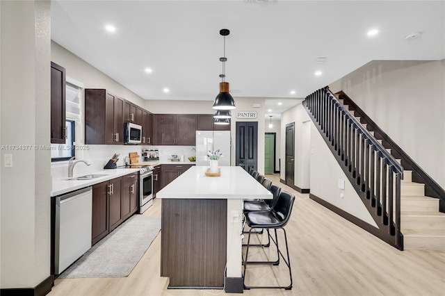 kitchen featuring a kitchen island, appliances with stainless steel finishes, pendant lighting, sink, and light hardwood / wood-style flooring