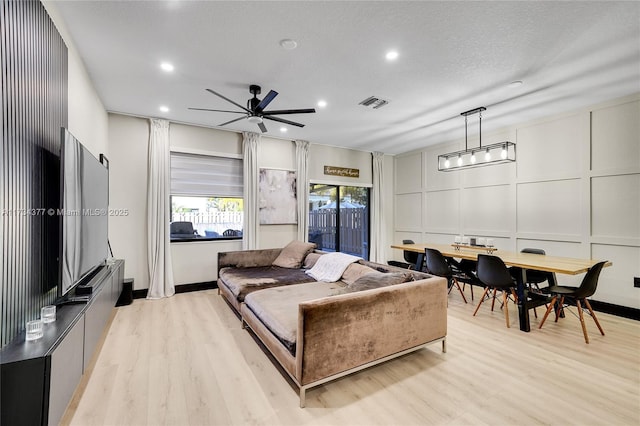 living room with ceiling fan, a textured ceiling, and light wood-type flooring