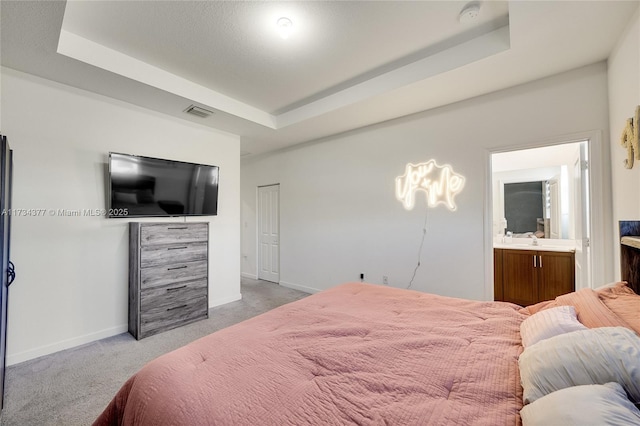 bedroom featuring light carpet, connected bathroom, and a tray ceiling