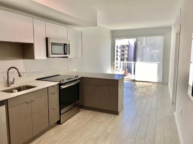 kitchen with gray cabinets, sink, light hardwood / wood-style floors, kitchen peninsula, and stainless steel appliances