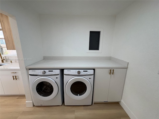 laundry room featuring sink, cabinets, washer and dryer, light hardwood / wood-style flooring, and electric panel