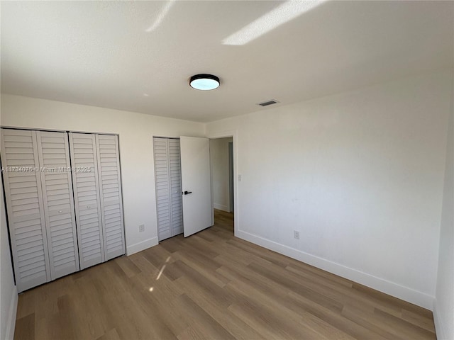 unfurnished bedroom with multiple closets and light wood-type flooring