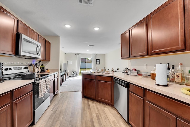 kitchen featuring appliances with stainless steel finishes, kitchen peninsula, sink, and light hardwood / wood-style flooring