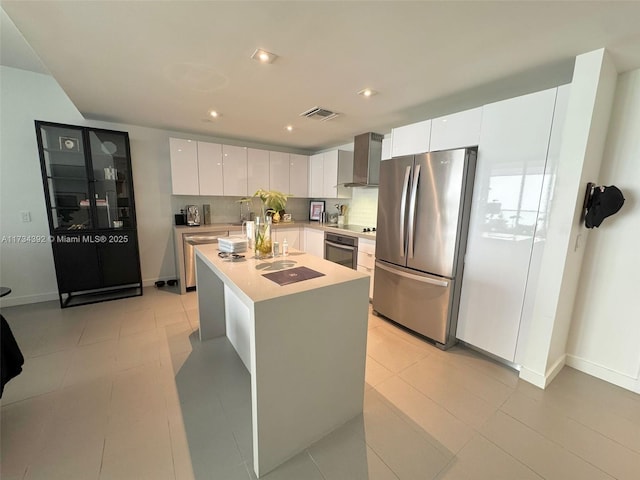 kitchen featuring appliances with stainless steel finishes, white cabinets, light tile patterned floors, a center island with sink, and wall chimney exhaust hood